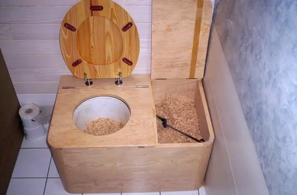 Photo de toilettes sèches d'intérieur avec bac à copeaux à côté de la cuvette.